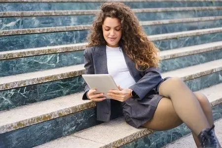 A Young Professional Woman Sitting on the Steps While Using a Tablet Device to Work
