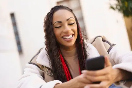 A Young Woman is Enjoying Her Time on Her Smartphone While Relaxing Outdoors Under the Sun