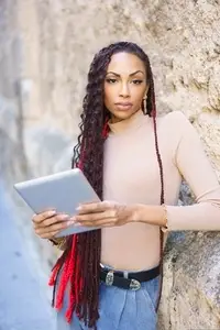 A Confident Young Woman Holding a Tablet while Posing in a Vibrant Urban Background Scene