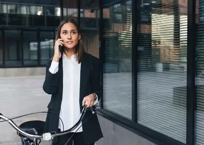 Confident female office worker with a bicycle talking on mobile phone outdoors