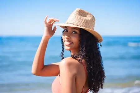 A Smiling Woman Wearing a Straw Hat Enjoying a Beautiful Day at the Beach with Joy A Smiling Woman Wearing a Straw Hat Enjoying a Beautiful Day at the Beach with Joy