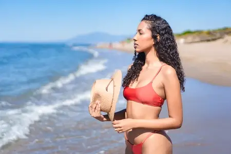 A Serene Beach Moment A Woman in a Stylish Bikini with a Straw Hat Relaxing by the Sea A Serene Beach Moment A Woman in a Stylish Bikini with a Straw Hat Relaxing by the Sea
