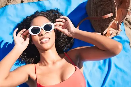 A Young Woman is Thoroughly Enjoying the Warm Sun on the Beach While Wearing Stylish Sunglasses