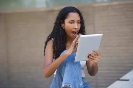 A Surprised Young Woman Engaged with a Tablet While Enjoying an Outdoor Setting Surrounded by Nature