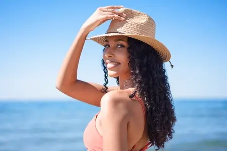 A Joyful Woman Wearing a Beautiful Straw Hat at the Beach  Enjoying the Warm Sunshine