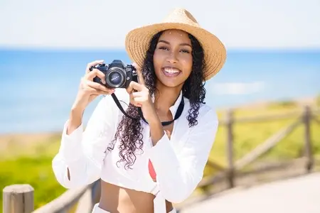 A Joyful Woman Taking Pictures with Her Camera on the Beautiful Beach on a Sunny Day