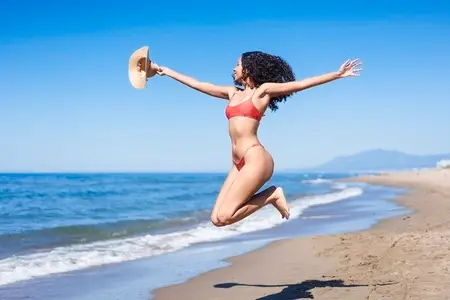 A Joyful Woman Happily Jumping on the Beach During a Bright and Warm Summer Day in Paradise