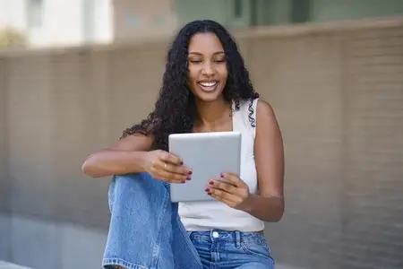 A Young Woman Engaged with a Tablet in a Bustling Urban Setting During Daylight Hours