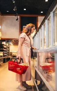 Full length of a young woman with a shopping cart standing at the fridge in a grocery store