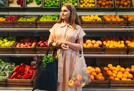 Female customer with bags full of vegetables and fruits standing in front of the shelves in the grocery store