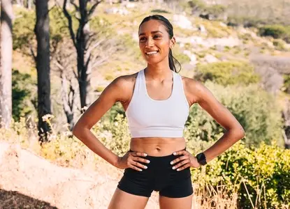 Young smiling female with hands on her hips  standing confidently ina  natural park during workout