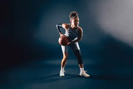 Professional female basketball player in uniform with ball over dark background in studio