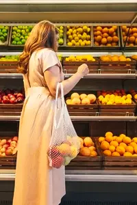 Back view of young woman choosing fruits while standing at shelves in grocery store