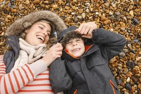 Happy mother and son in fur lined hoods laying on rocky beach