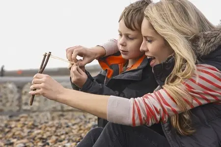 Mother teaching son how to use slingshot on rocky beach