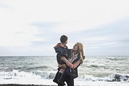 Happy carefree mother holding son on winter beach