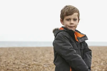 Portrait of cute boy in jacket on rocky winter beach