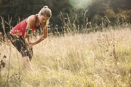 Female runner stretching leg in tall grass of summer meadow
