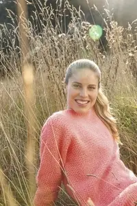 Portrait of beautiful blond woman in pink sweater sitting in sunny tall grass