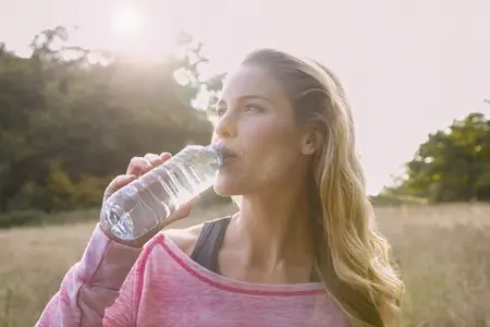 Beautiful thoughtful blond woman drinking from water bottle in sunny rural field