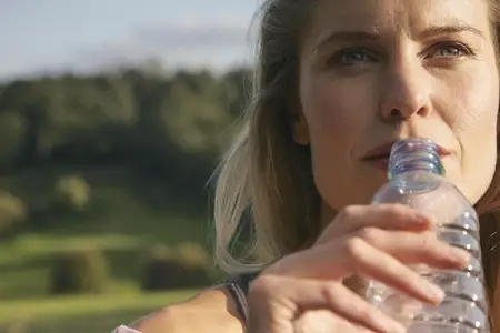 Close up portrait of beautiful thoughtful woman drinking from plastic water bottle in sunlight