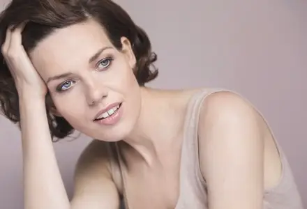Portrait of beautiful young brunette woman with blue eyes leaning and looking away with hand in hair