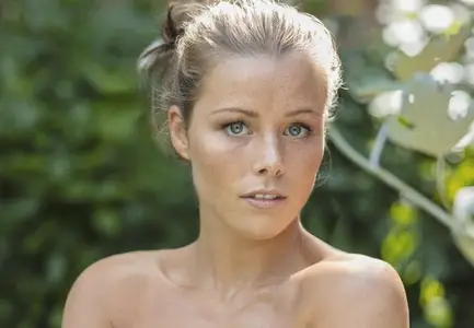 Portrait of beautiful wide eyed young woman with bare shoulders and freckles in summer garden