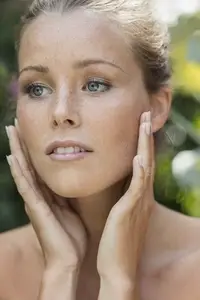 Close up portrait of beautiful young woman with freckles and blue eyes touching cheeks
