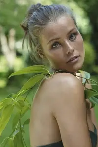 Portrait of beautiful young woman with green leaves draped over bare shoulder in summer garden