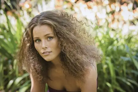 Portrait of beautiful young woman with curly brown hair and blue eyes in summer garden