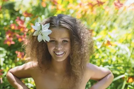 Portrait of beautiful young woman with bare shoulders in tropical garden with flower in curly hair