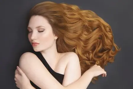 Portrait of beautiful serene young woman with long curly hair spread over gray background Portrait of beautiful serene young woman with long curly hair spread over gray background