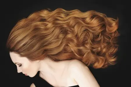 Studio portrait of beautiful young woman with long curly red hair against black background