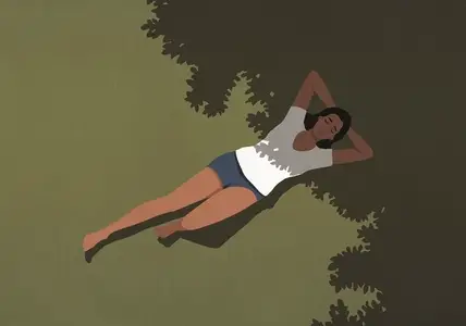 View from above of serene woman in shorts and t shirt laying in sunlight and shadow in summer grass