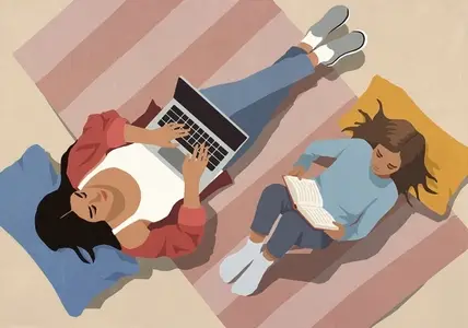 View from above of mother working at laptop next to daughter reading book on floor at home