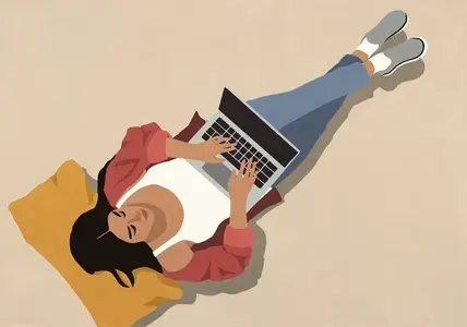 View from above of woman with pillow laying and working at laptop against beige background