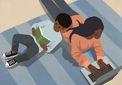 View from above son reading book leaning on mother working at laptop on rug