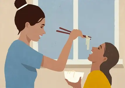 Happy mother feeding noodles to daughter with chopsticks by window at home