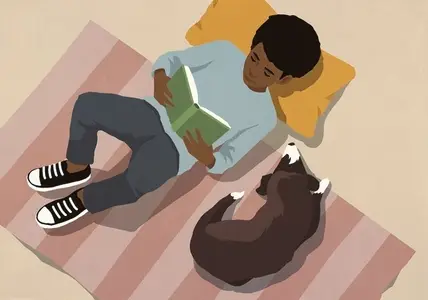 View from above of boy relaxing reading book on rug next to dog at home