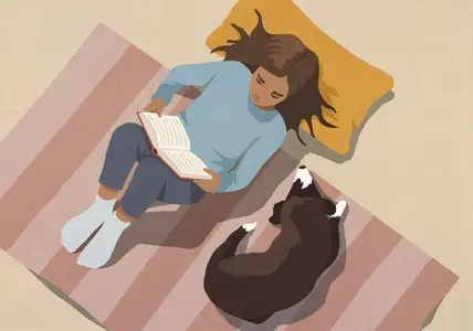 View from above of woman relaxing reading book next to dog on striped rug at home
