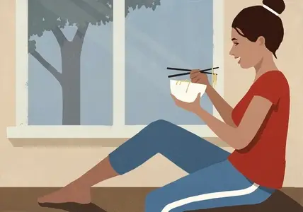 Happy woman eating Vietnamese pho noodles from bowl with chopsticks by window at home