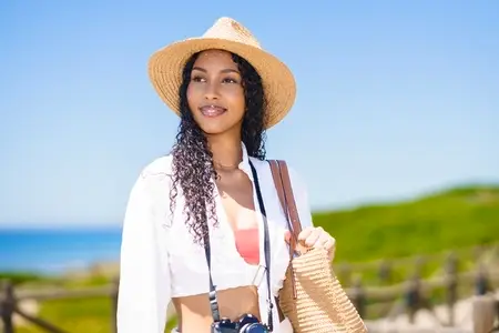 A Young Woman Embracing Summer Fashion at the Beach While Holding a Camera and Smiling