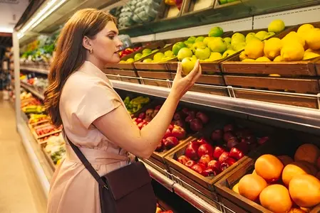 Female customer holding a green apple while standing in a grocery store