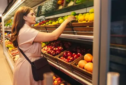 Young woman customer takes out a green apple from the shelf in the grocery store