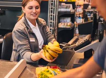 Cheerful female working as a cashier in a grocery store  holding bananas