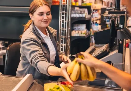 Smiling cashier gives bananas to a customer at the counter in a grocery store