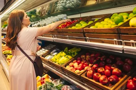 Young woman in casuals choosing bell pepper in the grocery store