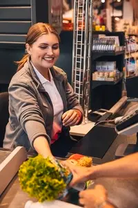 Smiling woman working as a cashier in grocery store sitting at the counter