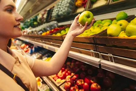 Woman holding an apple while choosing them in the grocery store on the shelves