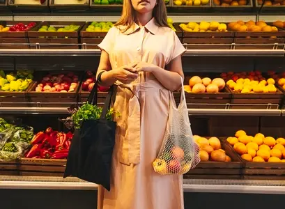 Cropped shot of a young woman with bags full of vegetables standing in front of shelves with fruits and vegetables Cropped shot of a young woman with bags full of vegetables standing in front of shelves with fruits and vegetables